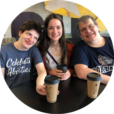 Three people sit at a table with coffee and smile