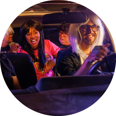 Four people smile in a car while wearing wigs