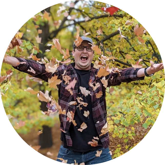 A man throws leaves into the air and smiles